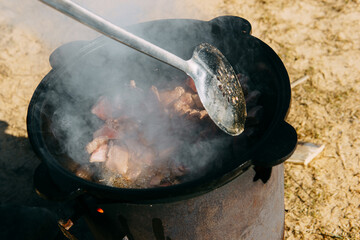 Meat cooking in a large cauldron outdoors over an open fire, a classic outdoor cooking concept for...