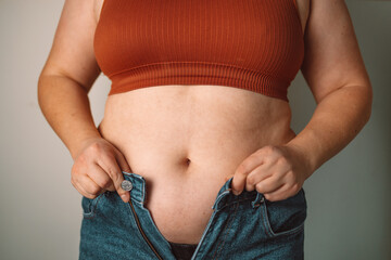 A woman trying to button up tight jeans, symbolizing challenges with body image and weight issues....