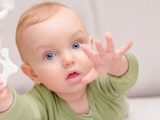 The baby reaches forward with his hand and looks at the camera