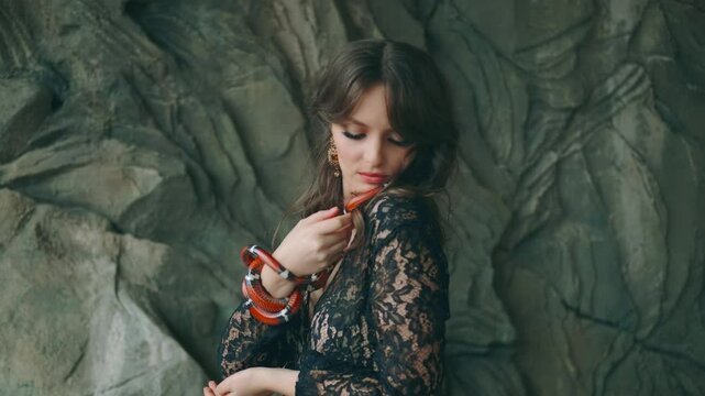 Portrait close-up female hands holding aspred red royal milk snake - sinaloa. Gothic fantasy woman dark queen of snakes and poison. girl vampire look at cute anaconda. black vintage medieval dress