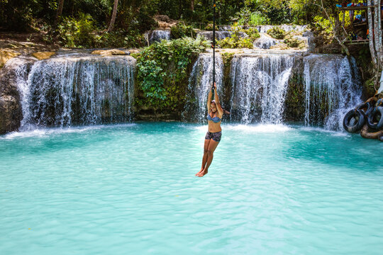 Young woman holding on to a rope swing over a waterfall, Siquijor island, Philippines