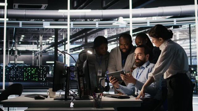 Data center system administrators performing maintenance on supercomputers used for AI processing. Team managing server hub rigs used for deep learning training, looking over business charts, camera A