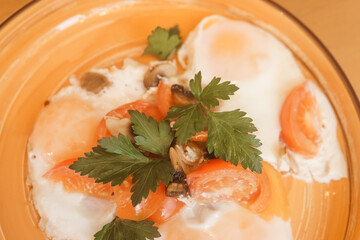 Freshly cooked delicious fried egg breakfast with chopped tomato, mushroom, and green parsley in orange bowl, top view. Healthy homemade meal.