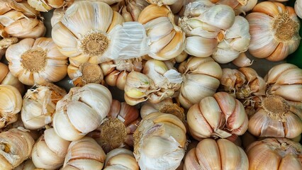 This is a close-up, overhead view of a large pile of garlic bulbs. The garlic bulbs vary slightly in size and have white to light brown papery skins, some of which are partially peeled or torn.