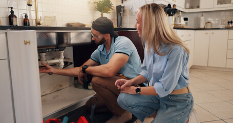 Plumber, man and woman by kitchen sink for pipe, inspection and check for leak for maintenance at house. People, handyman and client with assessment, repair and problem solving for drain at apartment