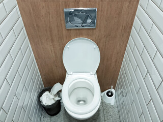 Public toilet, toilet bowl and full toilet paper basket. View from above.