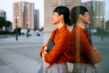 Japanese Businesswoman standing confidently outdoors in urban setting during golden hour with warm...