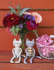 Soft fabric cats sit next to colorful flowers in a rustic setting