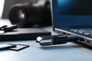 Flash drive connected to laptop and SD memory cards on gray textured table, closeup