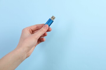 Woman holding USB flash drive on light blue background, closeup. Space for text