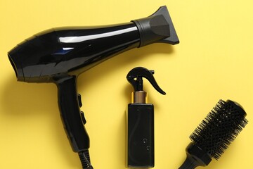 Different hairstyling tools on yellow background, flat lay