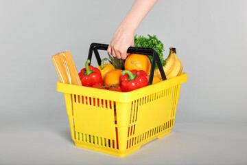 Woman with shopping basket full of products on gray background, closeup