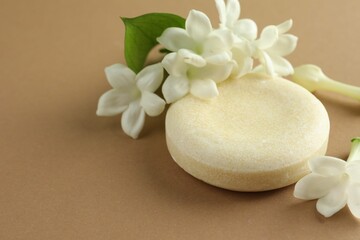 Bar of soap and jasmine flowers on light brown background, closeup. Space for text