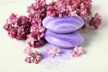 Soap bars, sea salt and lilac flowers on white table, closeup