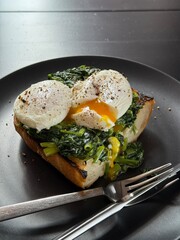 Poached egg on a piece of bread with spinach on the black plate
