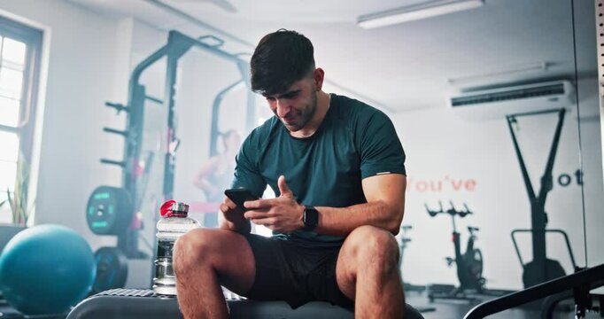 Break, fitness and man with phone in gym rest after exercise, training and workout routine. Sports, health club and happy person relax on smartphone for typing message, social media and connection