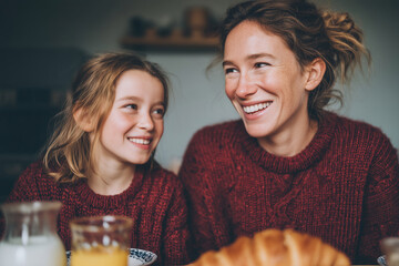 Happy mother and daughter sharing a joyful breakfast together at a cozy kitchen table, with pancakes, fruits, and coffee—capturing family bonding, warmth, and morning light in a loving home setting