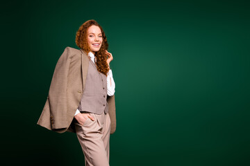 Stylish red haired businesswoman poses confidently in a fashionable suit against an elegant green...