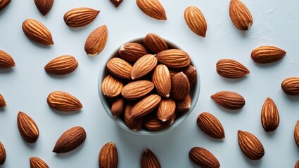 Almonds scattered around a bowl on a light blue surface.
