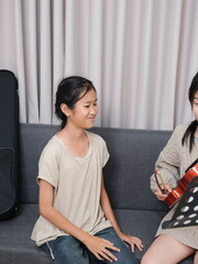 Fototapeta premium Two young girls are sitting on a couch, one of them playing a violin