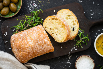 Ciabatta bread on wooden board with olive oil, olives and herbs.