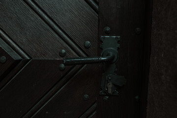 Detailed close-up of a dark wooden door with a black wrought iron handle and textured planks...