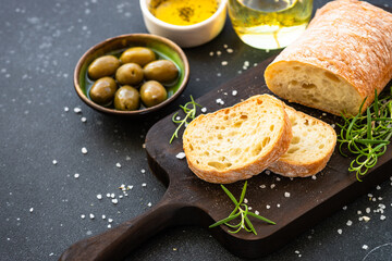 Ciabatta bread on wooden board with olive oil, olives and herbs.