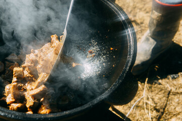 Pieces of meat frying in oil in a large cast iron cauldron with steam. Cooking outdoor in a big pot...