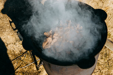 Pieces of meat frying in oil in a large cast iron cauldron with steam. Cooking outdoor in a big pot...