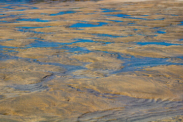 Yellow sand at low tide with small puddles of receding water, natural pattern on the beach