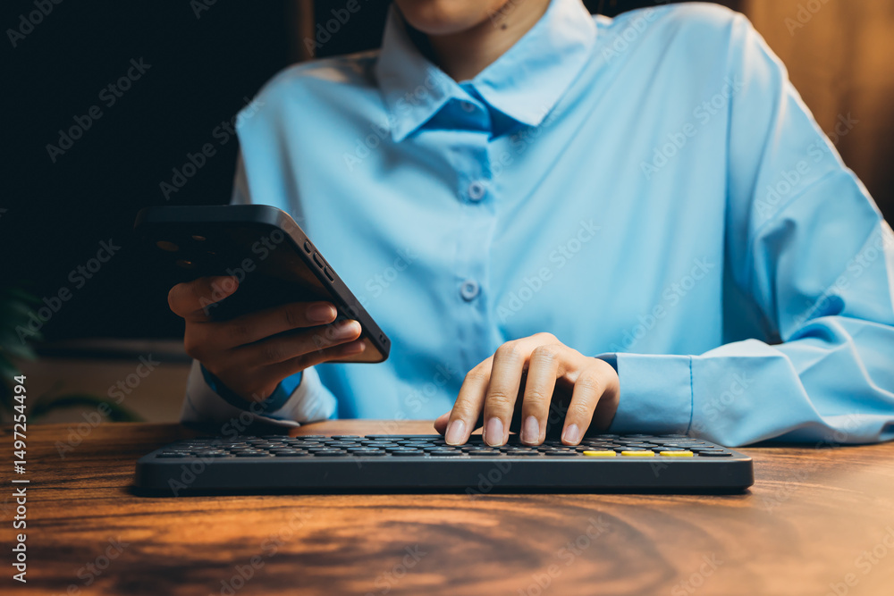 Poster person using smartphone while typing on keyboard in modern workspace with natural light background