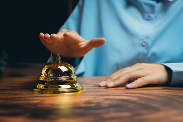 Hand Approaching Golden Bell on Wooden Desk in Hotel or Reception Setting