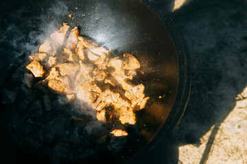Pieces of meat frying in oil in a large cast iron cauldron with steam. Cooking outdoor in a big pot...