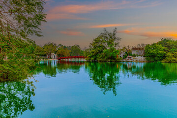 Fototapeta premium Lake in Hanoi Old Commercial Shops and Apartment house block in Hanoi Old Quarters Vietnam. Trees red bridge and green Pond 