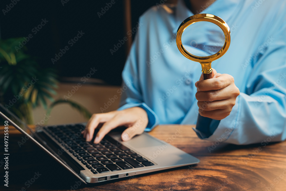 Poster person using magnifying glass while working on laptop computer in home office setting with green pla