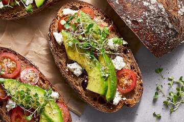 Sliced avocado and tomato on whole grain bread with sprouts  