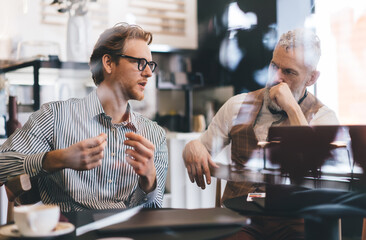 Two businessmen, one young and one older, discussing ideas during informal meeting in stylish...