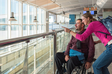 Man with disability using wheelchair with his female personal assistant is at the airport. They...