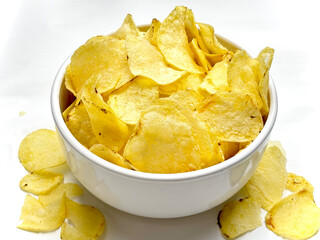 Potato chips in a white bowl viewed from above and potato crumbs on a white table