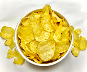 Potato chips in a white bowl viewed from above and potato crumbs on a white table
