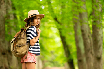 Adolescent hiker turns halfway toward camera, backpack secured, standing on woodland trail. Summer...