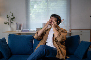 A man is sitting on a blue couch and talking on his cell phone
