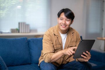 A man is sitting on a couch and pointing at a tablet