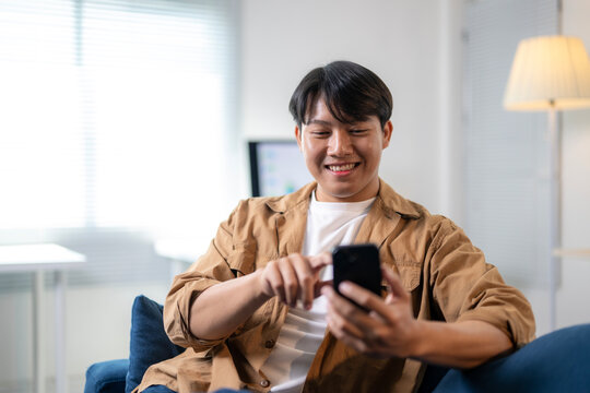A man is sitting on a couch and smiling while looking at his cell phone