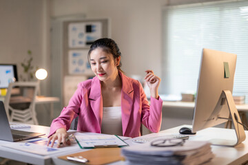 A woman in a pink jacket is sitting at a desk with a computer monitor