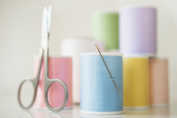 Studio shot of spools of pastel colored thread, needle and scissors
