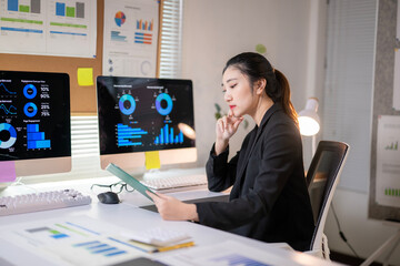 A woman is sitting at a desk with two computer monitors and a book