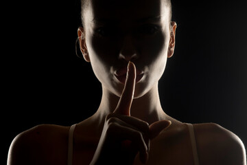 Mysterious silhouette of a woman making 'shh' gesture with finger on lips. Dark background with rim...