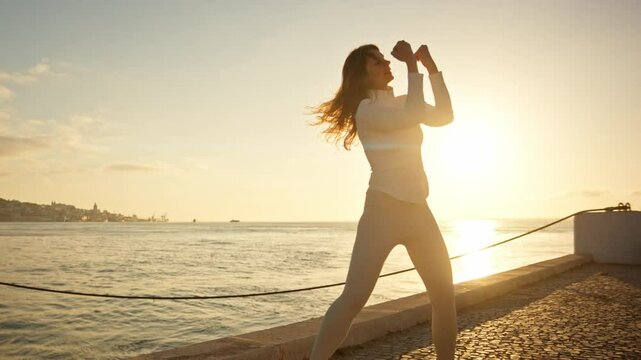 Woman practicing tai chi chuan at sunrise by the sea