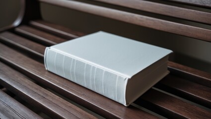 A wooden bench holds a white book that has no images